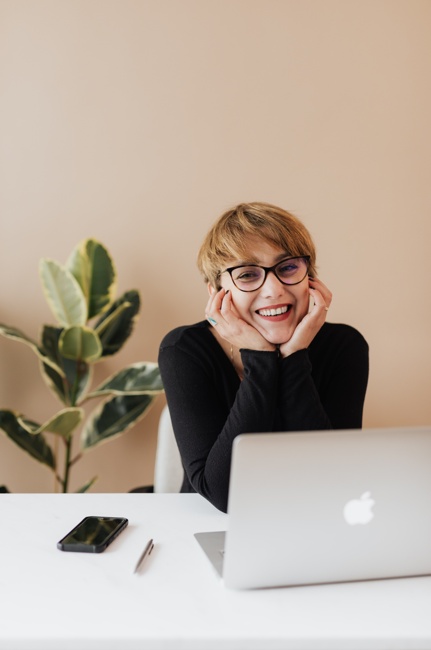 Photographie représentant une femme souriante devant son ordinateur portable dans un contexte neutre.